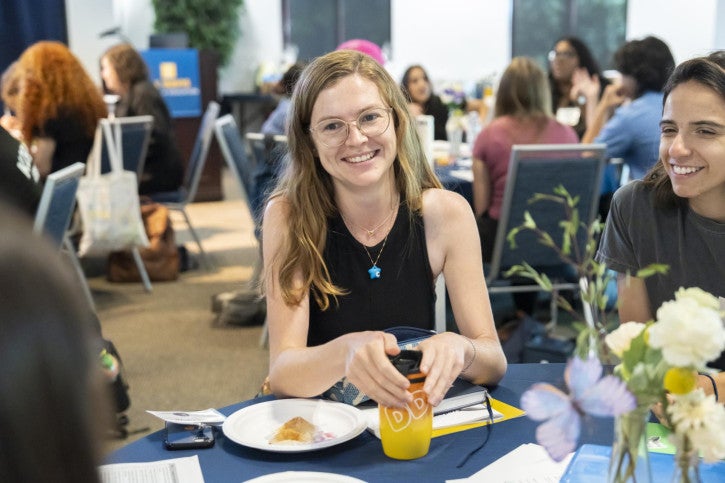 A woman seated at a table looks up and smiles.