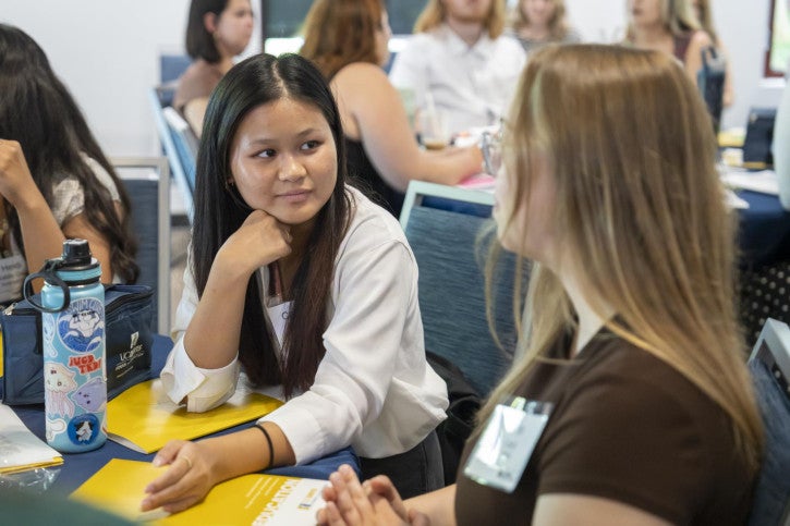 Two credential students converse with each other while seated at a table.