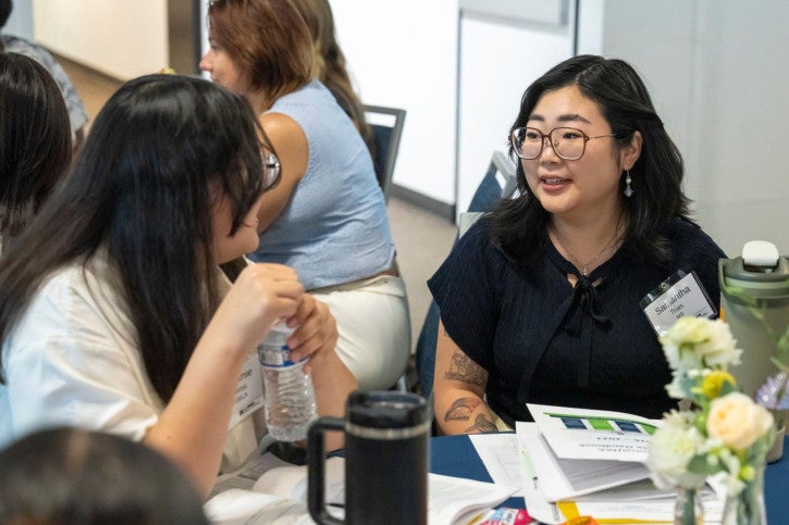 Two credential students sit at a table and speak to each other.