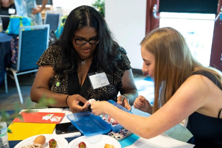 Two credential students sit at a table and put stickers onto envelopes.