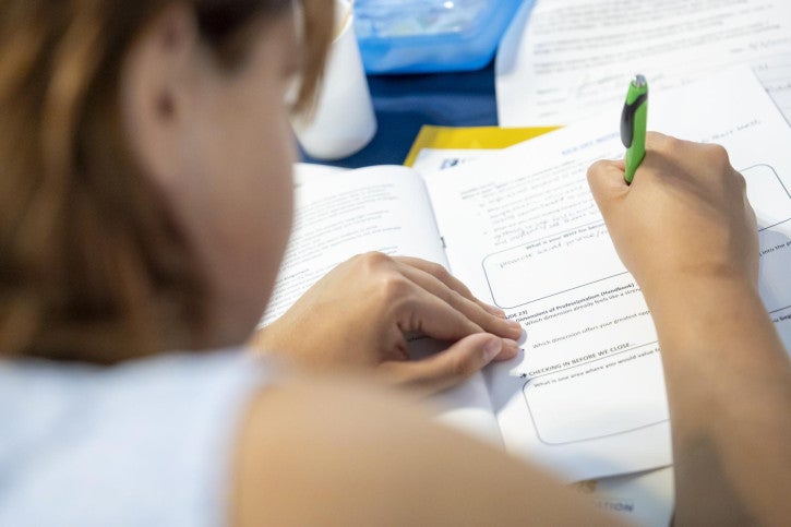A credential student looks down and writes in her program handbook.