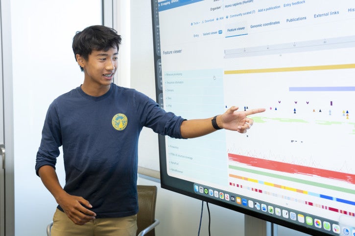 Linh smiles and points to data on a large screen.