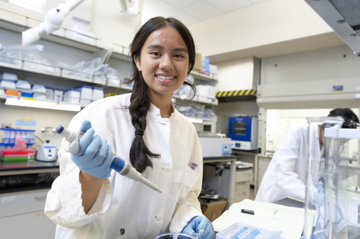 Nora smiles for the camera, holding a pipette.