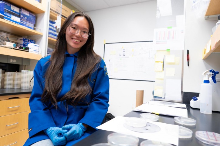 Oujen smiles for the camera, wearing a blue lab coat