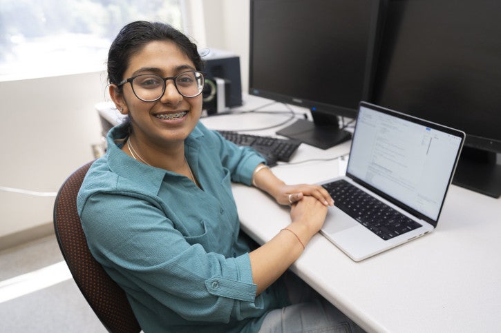 Prisha smiles next to a laptop.