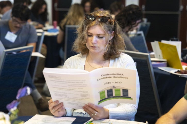 A student reads the program handbook while seated at her table.