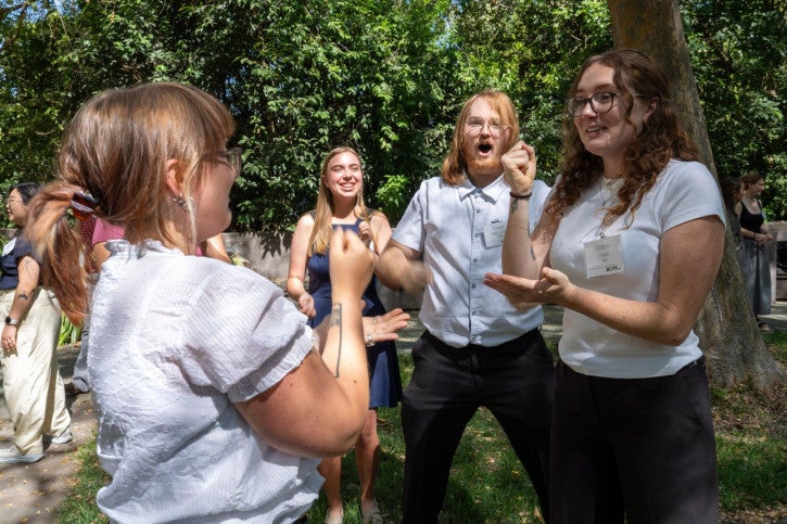 Four students gather around to face off in a game of Rock, Paper, Scissors.