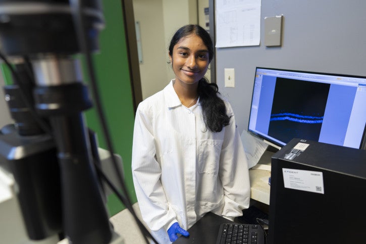 Sarayu smiles for the camera, surrounded by computer equipment.
