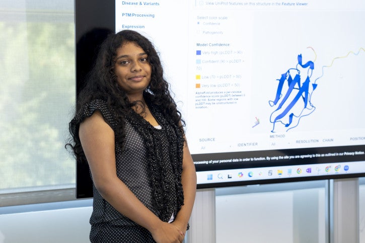 Shreeya smiles next to a screen with research data.