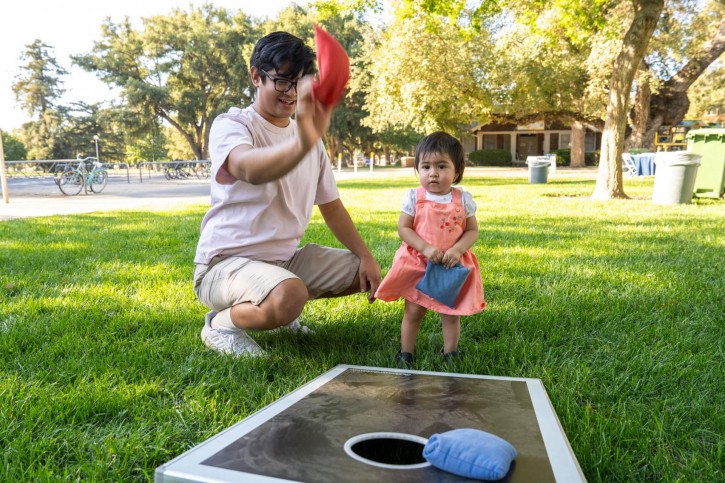 A parent and toddler play cornhole