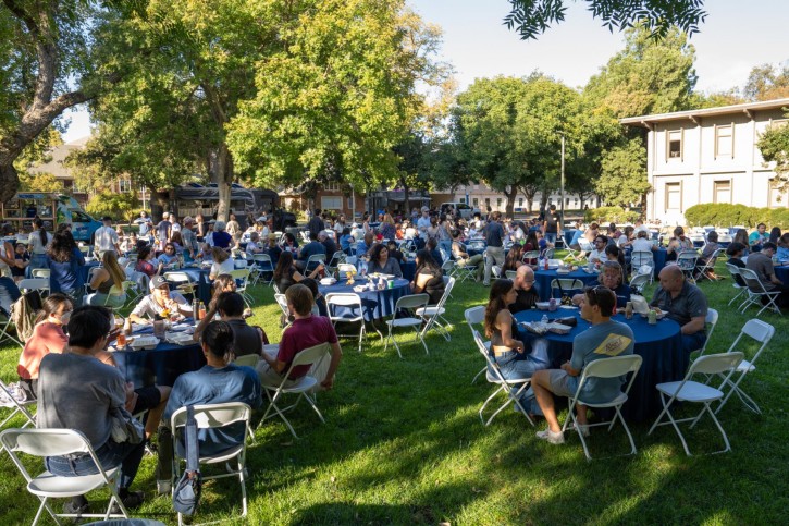 Wide shot of  people sitting at round tables on the Olson lawn