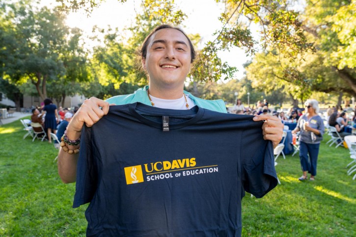 An attendee holds up their School of Education t-shirt and smiles