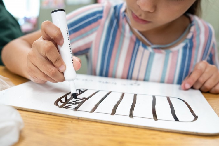 A young girl draws lines on a hand-held white board.