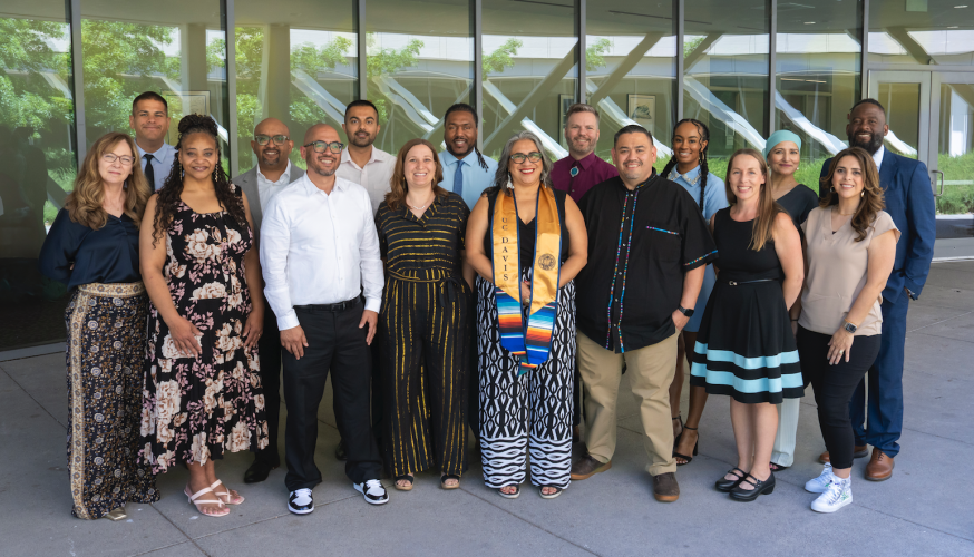 A group of 16 graduating men and women pose for a group photo.
