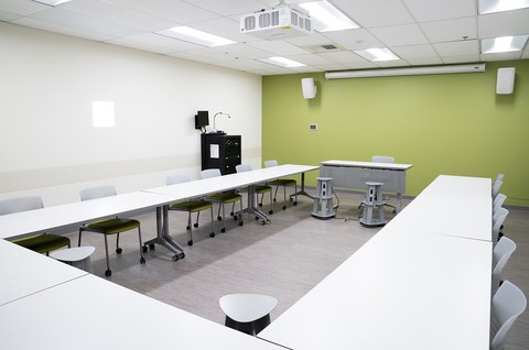 Brand new Sandi Redenbach and Ken Gelatt Learning Lab with bright white desks and an avocado green wall with a projector