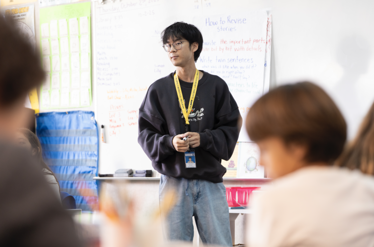 A teacher stands in front of his students who are facing the front of the classroom.