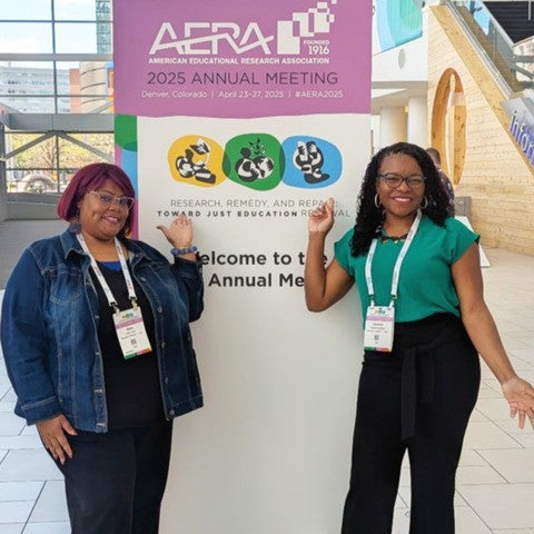 Two women pose for a photo while standing against a full-sized AERA conference banner.