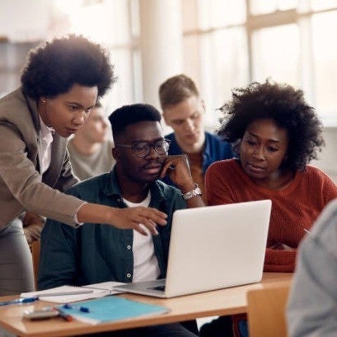 Three students gather around a table and look at a shared computer screen.