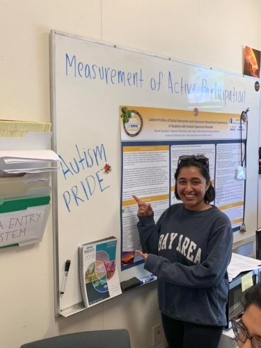 Someone gestures toward a whiteboard that reads "Autism Pride"