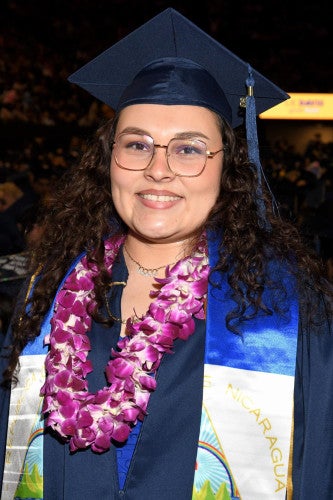 Alyss Foge wears glasses and graduation regalia and poses for a photo.