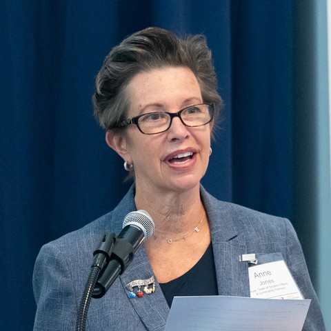 Anne Jones stands at podium, delivering a speech into a microphone