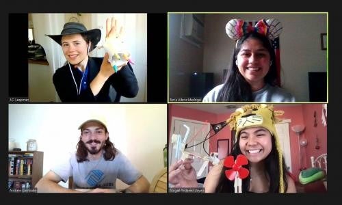 A screenshot of a video conference, where four people pose in four separate boxes. All of them are wearing costume hats and posing with crafts they created.