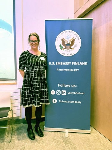 Cristina Buss stands next to a banner that says "U.S. Embassy,"