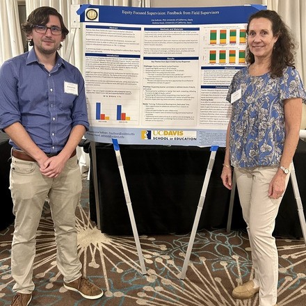 A man and woman stand in front of a research presentation poster.