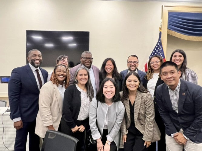 Several people wearing business casual clothing stand together and smile for a group photo.