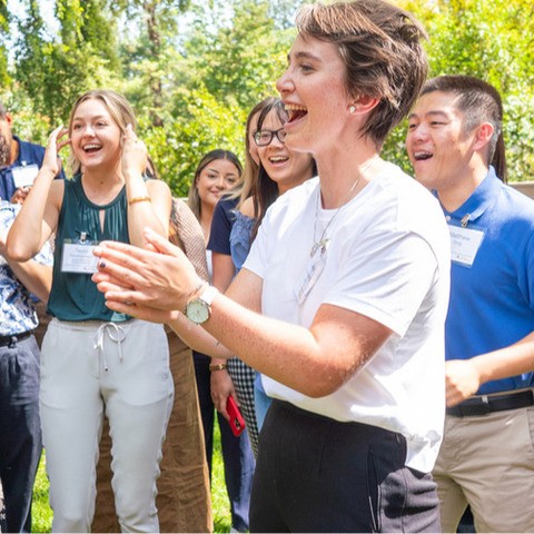 Students and faculty stand in a group outside, clapping and cheering