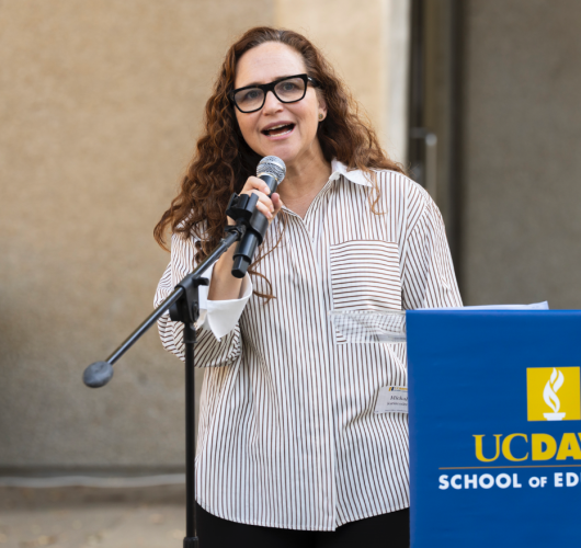 Michal Kurlaender stands at an outdoor podium and speaks into a microphone.