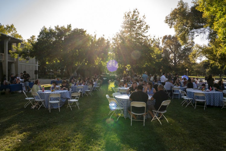 Attendees at 2025 Fall Welcome event sit at round tables with checked cloths, eating and talking