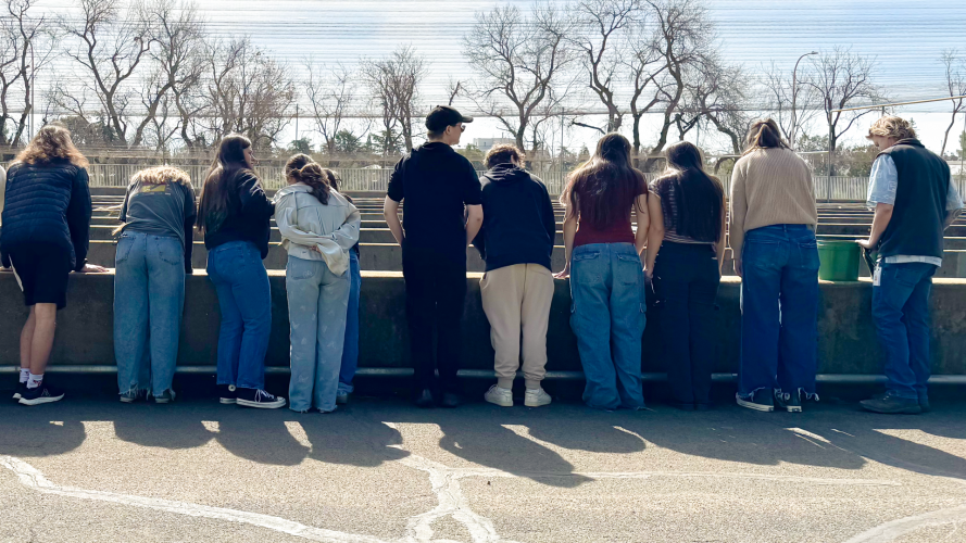 A line of high schoolers look over the edge of a salmon run at a fish hatchery.