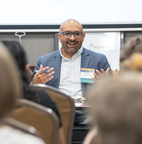 A CANDEL student sits at the front of a room and addresses an audience seated in front of him.