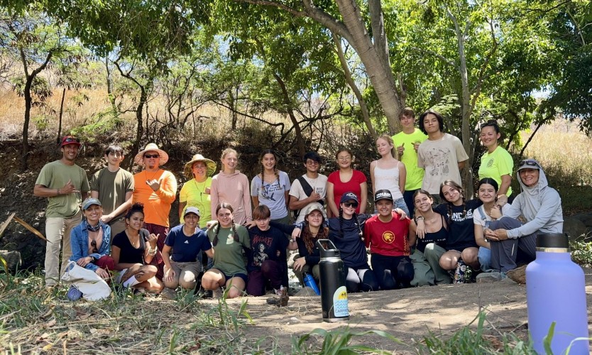 A group of students and adults pose together under a tree.