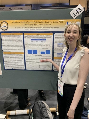 Caroline Van Zant poses for a photo in front of her poster that reads "Examining Student-Teacher Relationship Quality in School-Aged Students With and Without Autism"