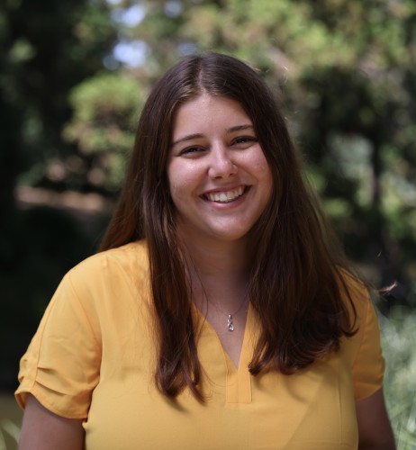 Carlie Rae Whiteman stands in the UC Davis Arboretum smiling in a yellow shirt