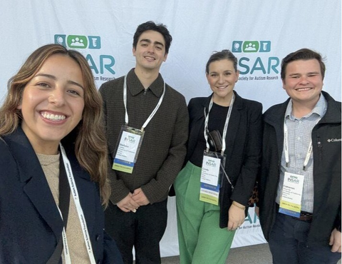Four people wearing professional clothing and lanyards pose for a selfie in front of a background screen that reads "INSAR."