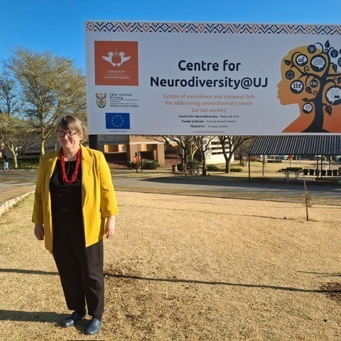 Lauren Lindstrom stands in front of a sign that says "Centre for Neurodiversity @UJ"