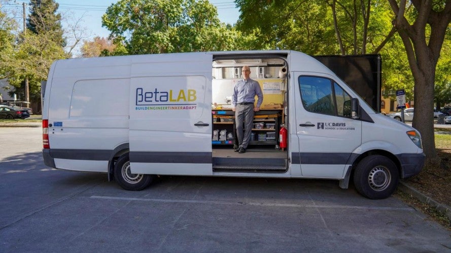 Associate Professor Lee Martin from the School of Education standing inside the Beta Lab maker van. Courtesy of Beta Lab Facebook. A white van with the words "Beta Lab" is parked with the sliding door open. Inside, Lee Martin leans against a counter and poses for a camera.