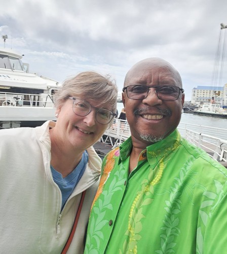 Lauren Lindstrom and Maximus Sefotho pose for a photo together in front of a boat and bay setting