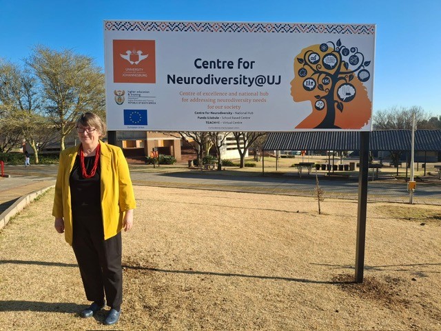 Lauren Lindstrom stands alone in front of a sign for the University of Johannesburg Centre of Neurodiversity