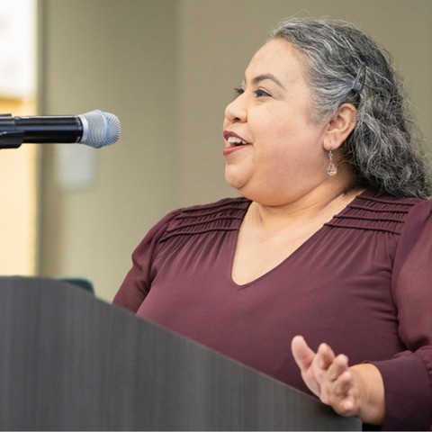 Marcela Cuellar stands at a podium and speaks into a microphone.