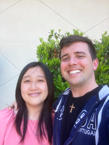 A man and woman pose for a selfie against a stucco wall.