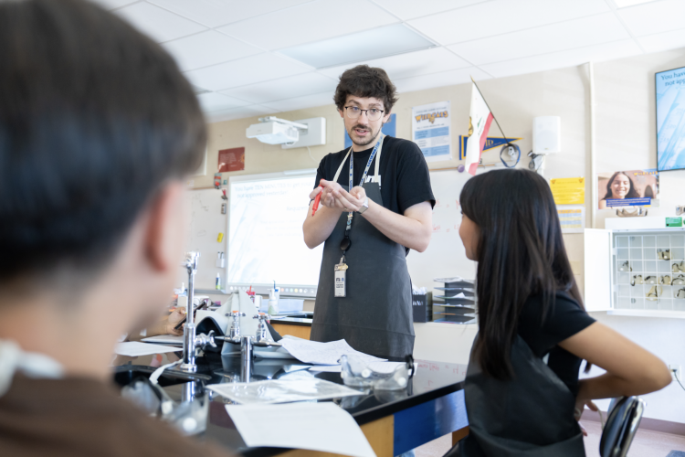 A science teachers addresses a group of students seated in front of him