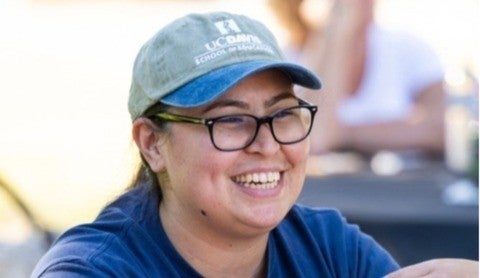 A woman wearing glasses and a School of Education baseball cap smiles and looks to her left