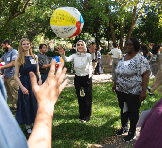 A credential student stands in a circle with others and throws a beach ball into the air. Arms reach out to grab it.