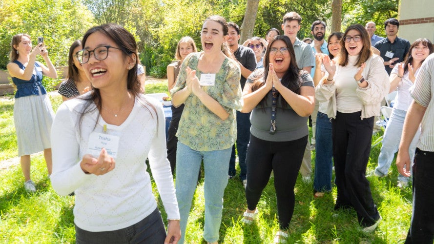 A group of credential students stand in a group, laugh, and cheer.