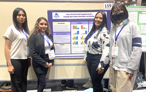 Four women pose for a photo in front of a conference poster that reads "A Day in the Life of Dual Language Learners: Language Input-Output, Interactions, and Activities"