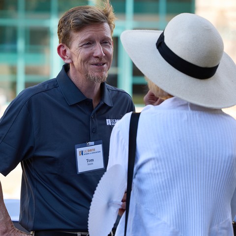 Tom Smith smiles at a woman who is facing away from the camera, talking to him.